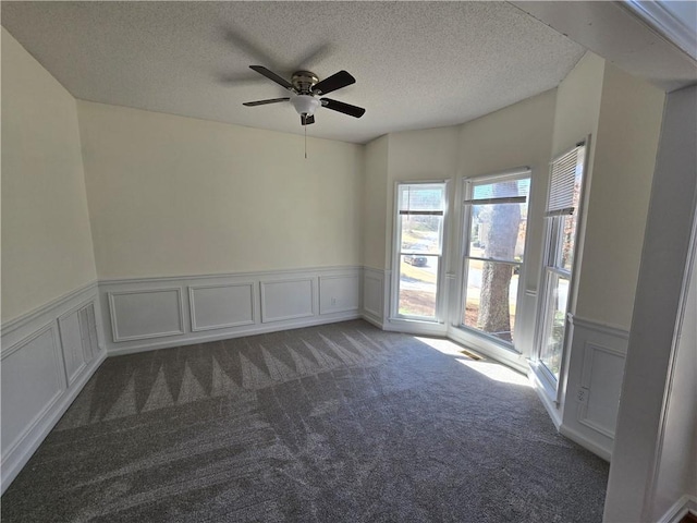 unfurnished room featuring a textured ceiling, wainscoting, and carpet