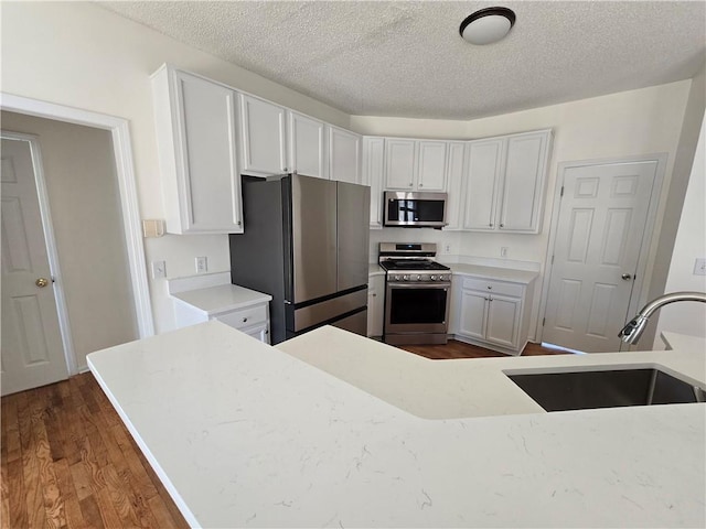 kitchen with dark wood finished floors, stainless steel appliances, light countertops, white cabinetry, and a textured ceiling