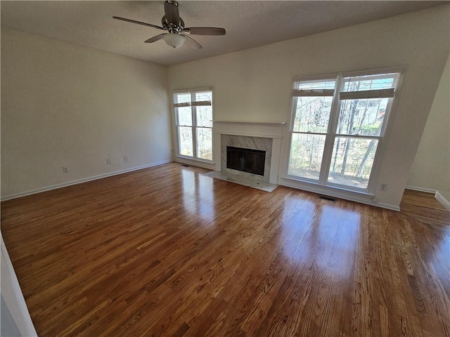 unfurnished living room featuring ceiling fan, dark wood-style flooring, a high end fireplace, and visible vents