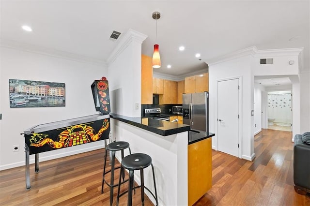 kitchen with appliances with stainless steel finishes, a breakfast bar, light brown cabinetry, decorative light fixtures, and kitchen peninsula