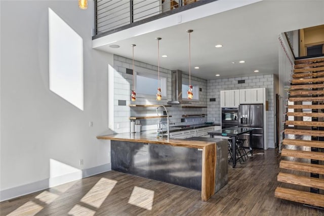 kitchen with dark wood-style floors, wall chimney exhaust hood, fridge with ice dispenser, and backsplash