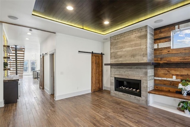 unfurnished living room featuring a large fireplace, a raised ceiling, wood ceiling, a barn door, and wood finished floors
