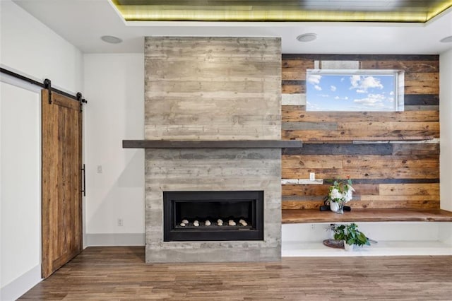 unfurnished living room featuring a large fireplace, a barn door, and wood finished floors