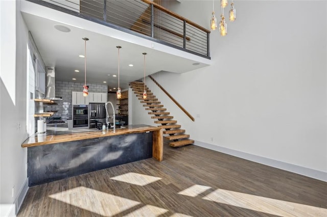 bar with wall chimney exhaust hood, a sink, stairway, and wood finished floors