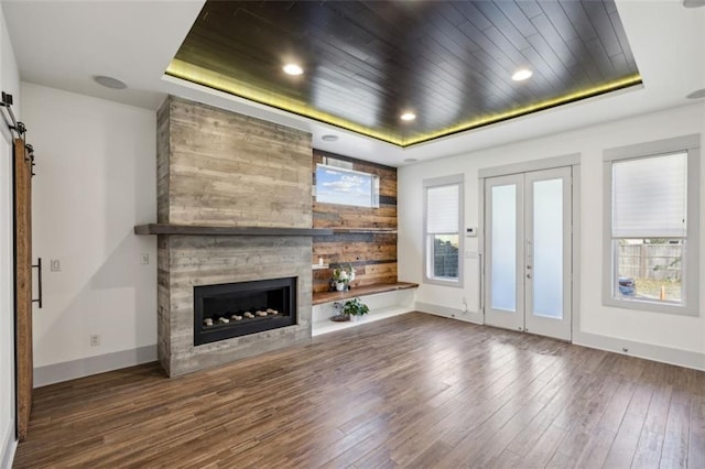 unfurnished living room featuring a raised ceiling, wooden ceiling, a fireplace, and a barn door