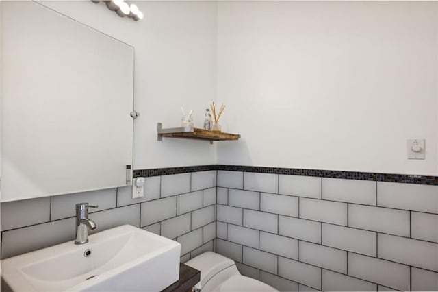 bathroom with a sink, toilet, and tile walls