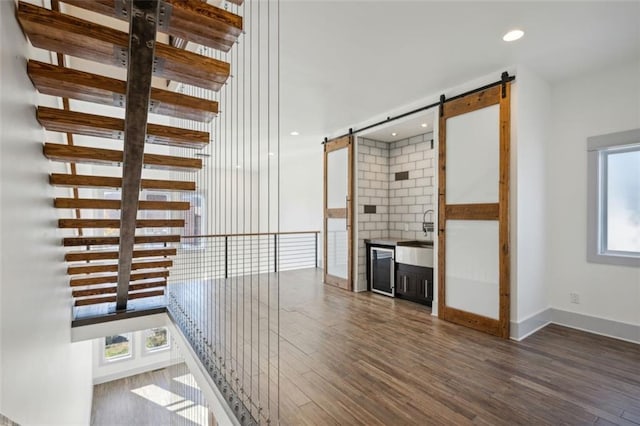 corridor with recessed lighting, baseboards, a barn door, and wood finished floors