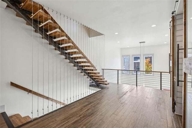 staircase with a barn door, wood finished floors, and recessed lighting