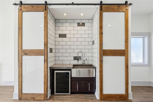 bar featuring light wood-style floors, beverage cooler, a sink, and a barn door