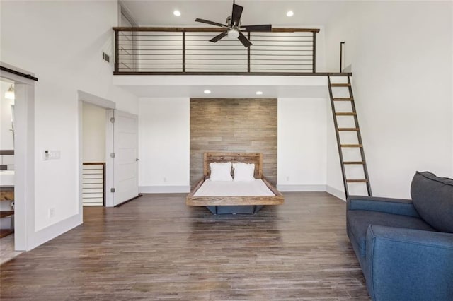 unfurnished bedroom with recessed lighting, a high ceiling, a barn door, wood finished floors, and baseboards