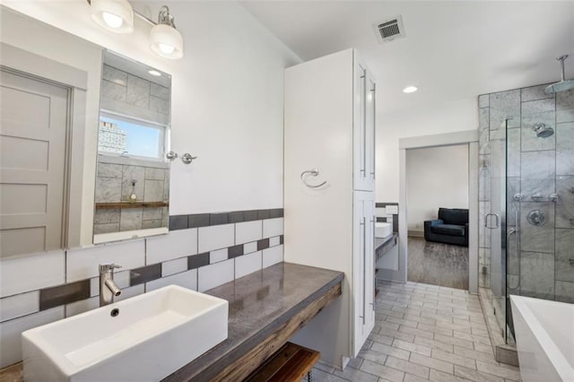 full bath featuring tile walls, a sink, a stall shower, a tub to relax in, and visible vents