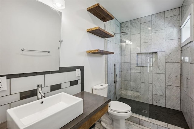 full bath with a tile shower, a sink, toilet, and tile walls