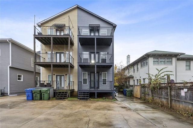 rear view of house featuring a balcony, covered porch, and fence