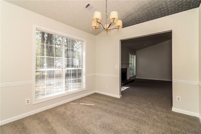 spare room featuring a textured ceiling, visible vents, baseboards, an inviting chandelier, and dark carpet
