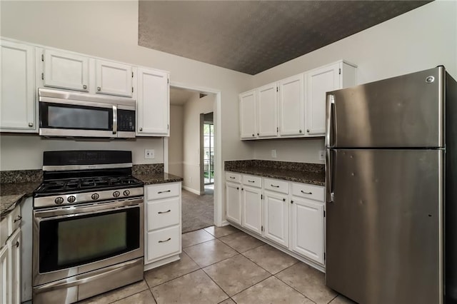 kitchen with appliances with stainless steel finishes, dark stone countertops, white cabinetry, and light tile patterned floors