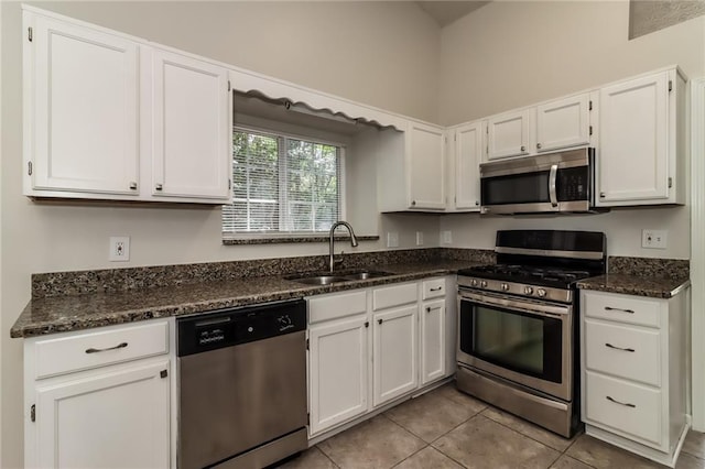 kitchen with dark stone countertops, a sink, light tile patterned floors, white cabinetry, and appliances with stainless steel finishes