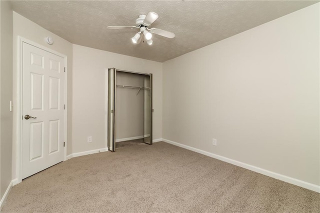 unfurnished bedroom featuring light carpet, a textured ceiling, baseboards, a closet, and ceiling fan