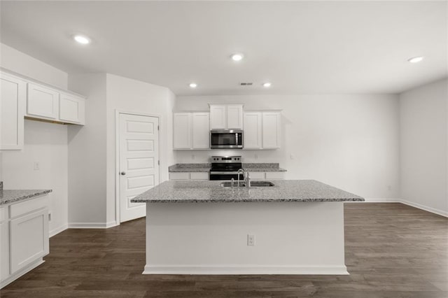 kitchen with stainless steel appliances, light stone countertops, a center island with sink, and white cabinets