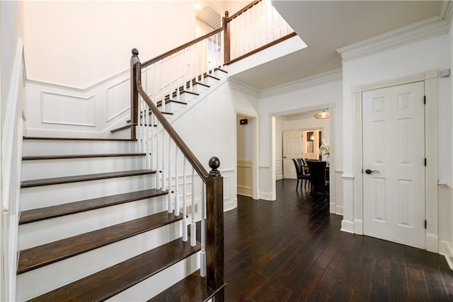 stairs with wood-type flooring, a decorative wall, crown molding, and wainscoting