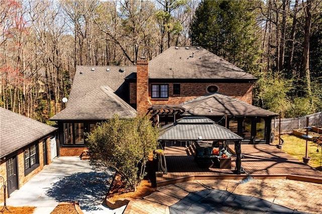rear view of house featuring driveway, roof with shingles, a chimney, fence, and a deck