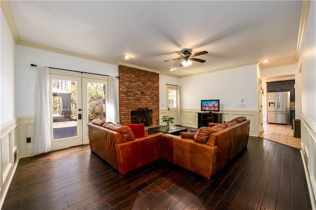 living area featuring a wainscoted wall, crown molding, a ceiling fan, wood finished floors, and a brick fireplace