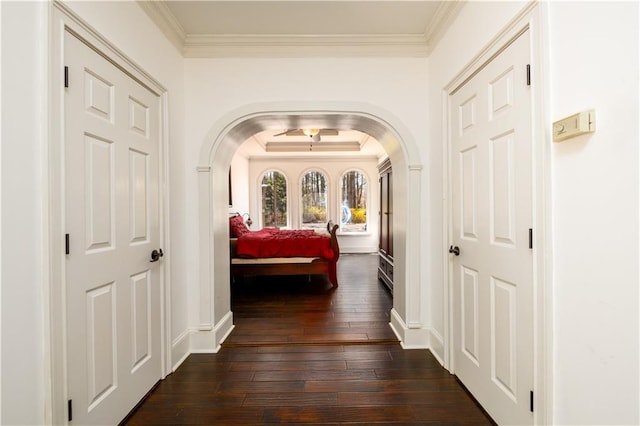 hallway with dark wood finished floors, baseboards, arched walkways, and ornamental molding