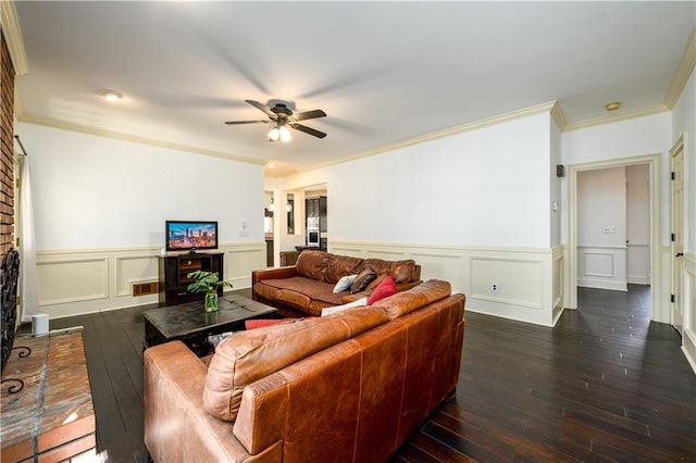 living area with wood-type flooring, a ceiling fan, ornamental molding, and a brick fireplace