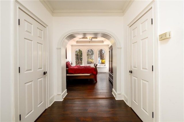 hallway with dark wood-style floors, crown molding, arched walkways, and baseboards