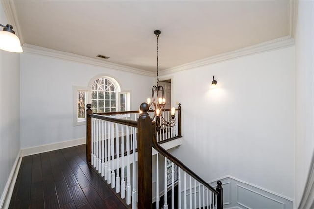 stairs with hardwood / wood-style floors, baseboards, visible vents, crown molding, and a notable chandelier