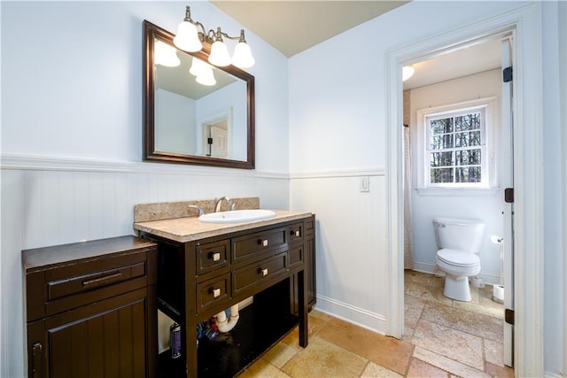 bathroom featuring baseboards, toilet, stone tile flooring, vanity, and an inviting chandelier
