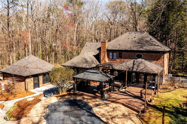 view of front of house with fence, roof with shingles, a gazebo, a view of trees, and a chimney