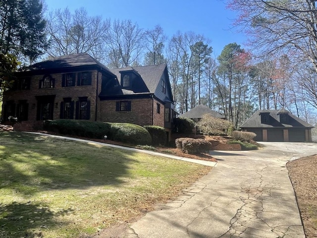 view of side of home featuring an outdoor structure, concrete driveway, a detached garage, brick siding, and a yard