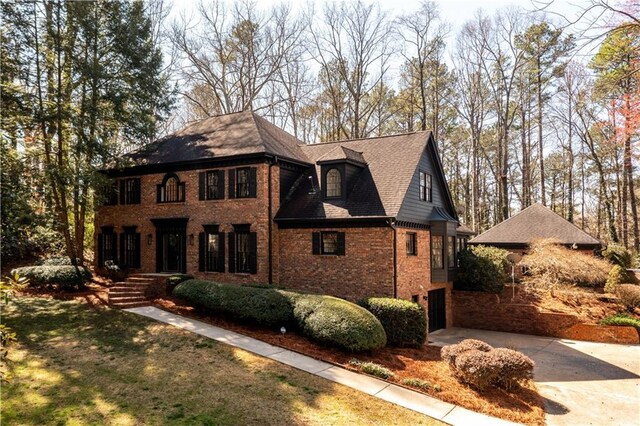 view of front facade with driveway, brick siding, a front lawn, a shingled roof, and a garage