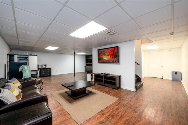 living area with visible vents, baseboards, stairway, a drop ceiling, and wood finished floors