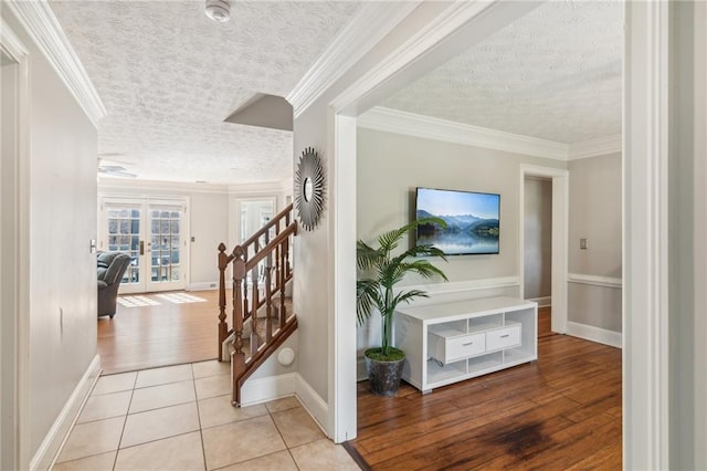 tiled foyer entrance featuring a textured ceiling, french doors, stairs, baseboards, and crown molding