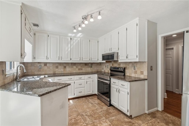kitchen featuring appliances with stainless steel finishes, a sink, white cabinets, and dark stone countertops
