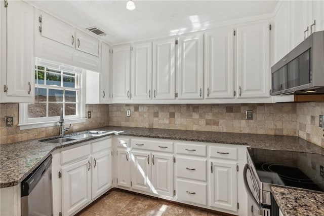 kitchen with appliances with stainless steel finishes, white cabinetry, a sink, and dark stone countertops