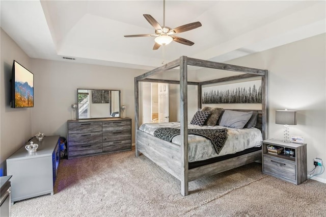 carpeted bedroom with a raised ceiling and a ceiling fan