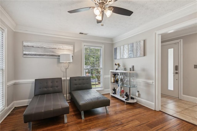 living area featuring wood finished floors, a ceiling fan, a textured ceiling, ornamental molding, and baseboards