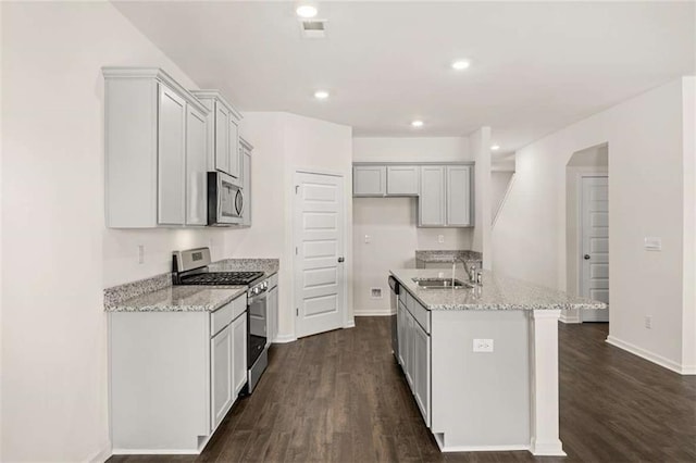 kitchen featuring a center island with sink, sink, light stone countertops, appliances with stainless steel finishes, and dark hardwood / wood-style flooring