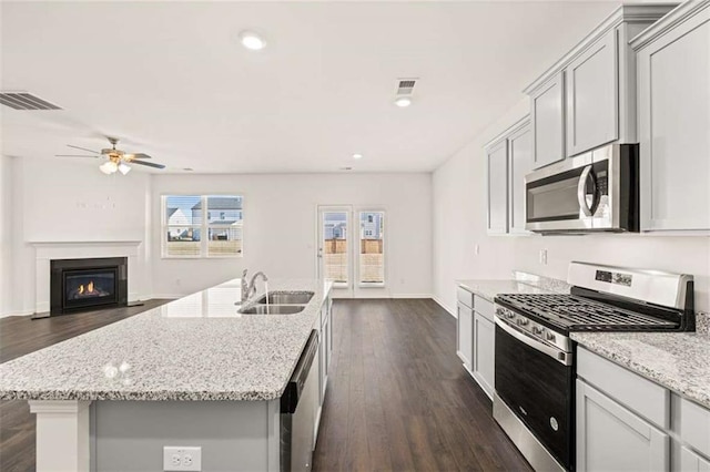 kitchen with appliances with stainless steel finishes, a center island with sink, light stone counters, and sink