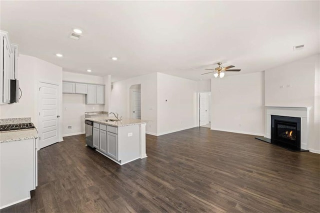 kitchen with ceiling fan, dishwasher, light stone countertops, sink, and an island with sink