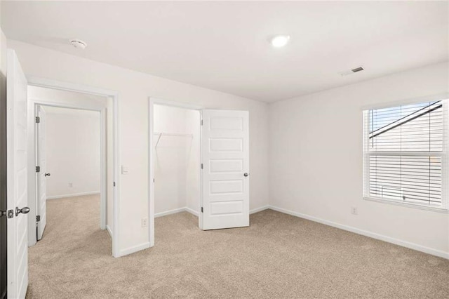 unfurnished bedroom with a walk in closet, light carpet, and a closet