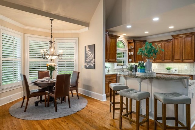 dining room featuring baseboards, a chandelier, crown molding, light wood finished floors, and lofted ceiling