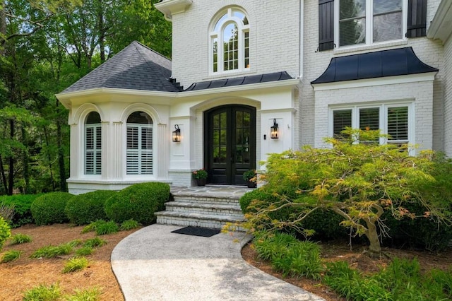 property entrance featuring french doors, a standing seam roof, brick siding, and metal roof