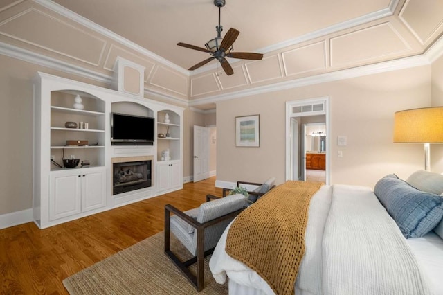bedroom featuring a fireplace, ornamental molding, wood finished floors, ceiling fan, and baseboards