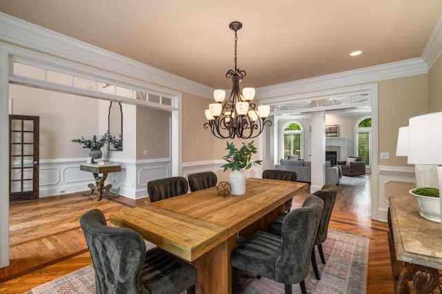 dining area featuring a chandelier, a wainscoted wall, ornamental molding, and a fireplace