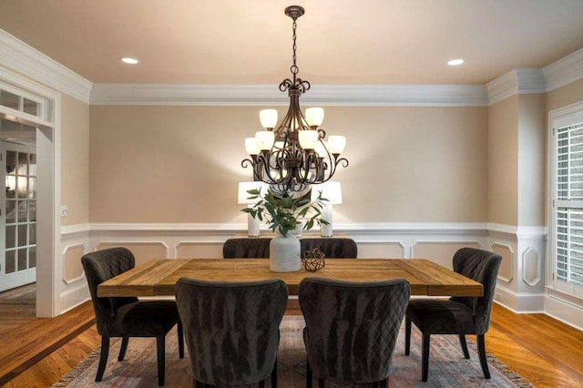 dining space with a chandelier, ornamental molding, wainscoting, wood finished floors, and a decorative wall