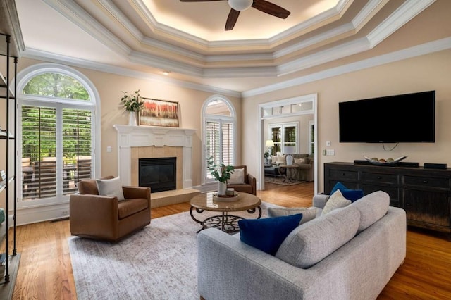 living room featuring ornamental molding, a raised ceiling, a ceiling fan, a fireplace, and wood finished floors