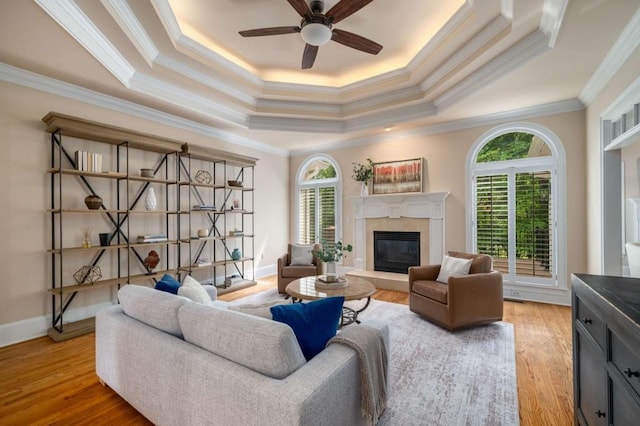 living area featuring a tray ceiling, plenty of natural light, a tile fireplace, crown molding, and ceiling fan
